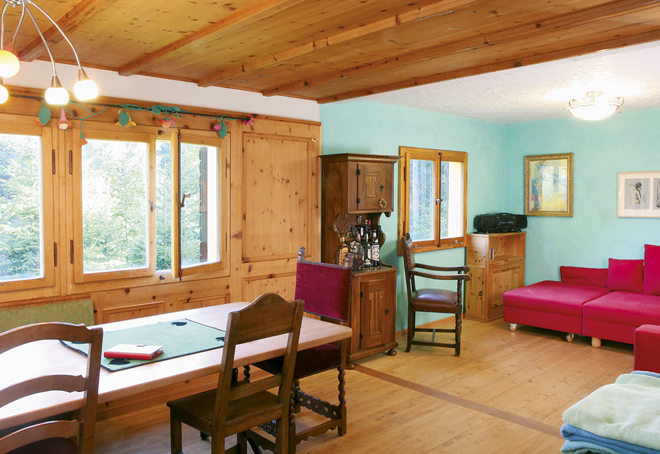Die Stube des Waldfrieden Ferienhauses verfügt über einen grossen Holztisch und eine Eckbank sowie ein rotes Sofa.